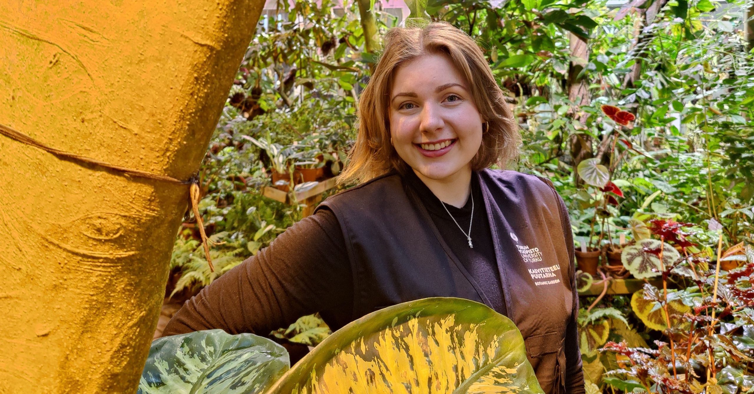 Nuori nainen hymyilee Turun yliopiston biodiversiteettiyksikön kasvitieteellisellä puutarhalla.